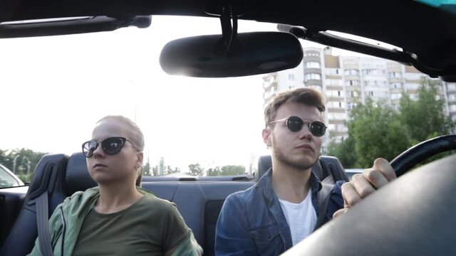 young couple in sunglasses ride in a convertible car around the city in summer.