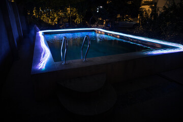 Pool and waterfall at night - vacation background. Colorful light decoration. Freezelight