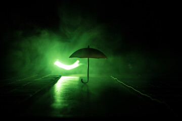 Silhouette of umbrella miniature on table with dark toned foggy background. Creative concept.