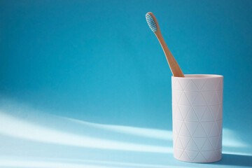 Eco friendly bamboo toothbrush in white holder on blue background with free space for text. Dental care and teeth treatment concept. Copy space.