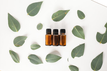 Flat lay image of three amber essential oil bottles surrounded by eucalyptus gum leaves