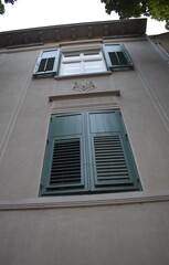 Windows on the old villa with dark green window linings. Gray concrete facade.