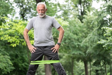 Naklejka na ściany i meble Senior sportsman exercising for glutes using resistance band at park