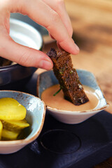 A woman's hand dips a piece of black bread into the sauce