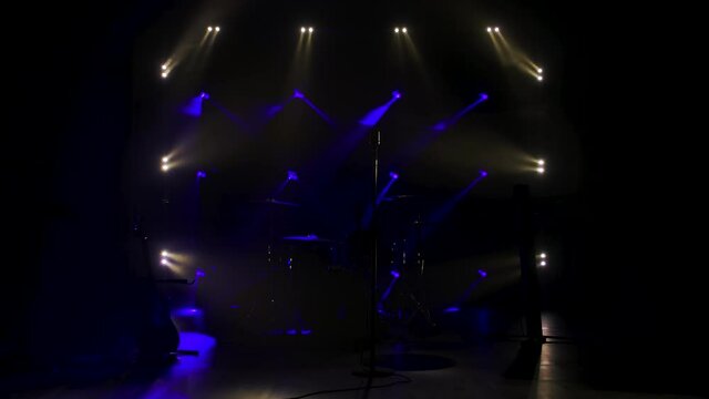 Classic retro chrome microphone and electric guitar together with drums and piano synthesizer keyboard on the stage in dark studio with smoke and neon lighting. Dynamic blue neon lighting effects