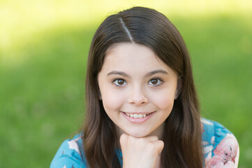 Little girl with long hair relaxing in park sunny day green grass background, adorable smile concept