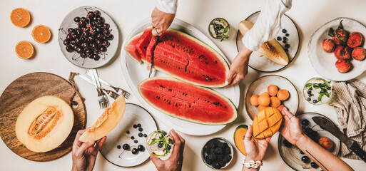 Summer tropical fruit party table. Flat-lay of lunch with fruit, berries, watermelon, lemonade and peoples hands over white background, top view. Vegan, clean eating, fruiterian food concept