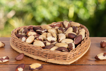 Brazilian nut, known as "Castanha do Pará" in a heart-shaped basket on a wooden table with an unfocused garden background.