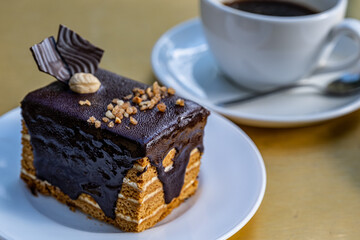 A large piece of honey cake drenched in chocolate with a cup of coffee. puff chocolate marquise.