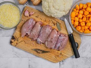 meat with vegetables
Boneless chicken thighs on a wooden board with vegetables, spices and grated cheese. Close-up top view.