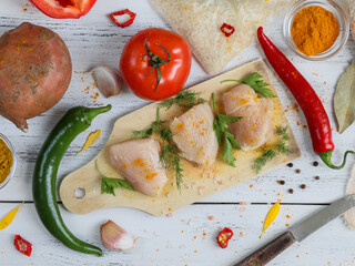 Chicken fillets are on the board.
Three pieces of chicken fillet lie on a board, and around vegetables, spices, rice in a bag and a knife. Close-up top view.