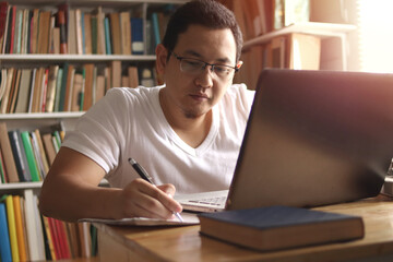 Asian muslim man studying in library, exam preparation concept. Male college student using laptop to learn online