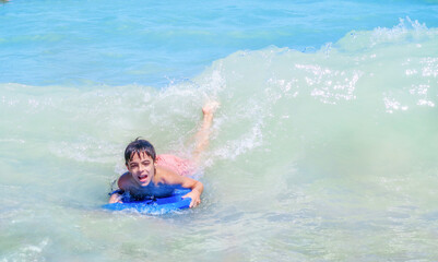 child bodyboarding a wave in a blue sea with an expression of fun and happiness on his face  