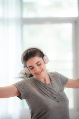Naklejka premium Happy young woman in headphones is listening to music, relax dancing and smiling in bedroom at home