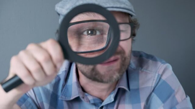a curious funny surprised Middle-aged  man in cap who is looking at the camera through a magnifying glass. Humorous portrait