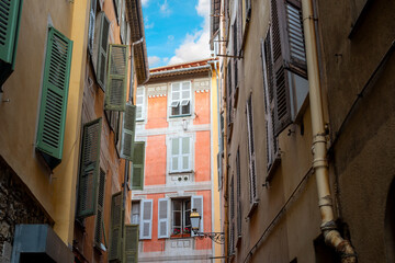 Fototapeta na wymiar A colorful, historic apartment building under a blue sky is seen on a narrow street in old town Vieux Nice, France.