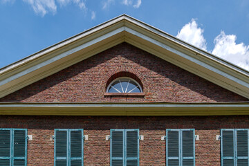 Beautiful vintage exterior of top of building with old rough brick wall facade and elegant windows which consist of wooden green shutters and gable roof against blue sky.