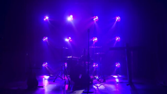 Classic retro chrome microphone and electric guitar together with drums and piano synthesizer keyboard on the stage in dark studio with smoke and neon lighting. Dynamic colored neon lighting effects