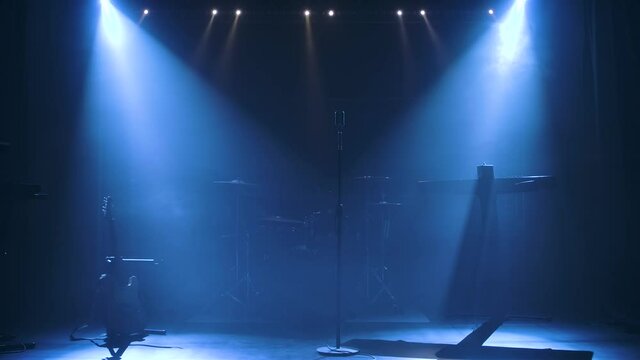 Classic retro chrome microphone and electric guitar together with drums and piano synthesizer keyboard on the stage in dark studio with smoke and neon lighting. Dynamic colored neon lighting effects