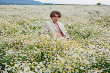 Tall handsome man sitting on a white chair in camomile flowers field