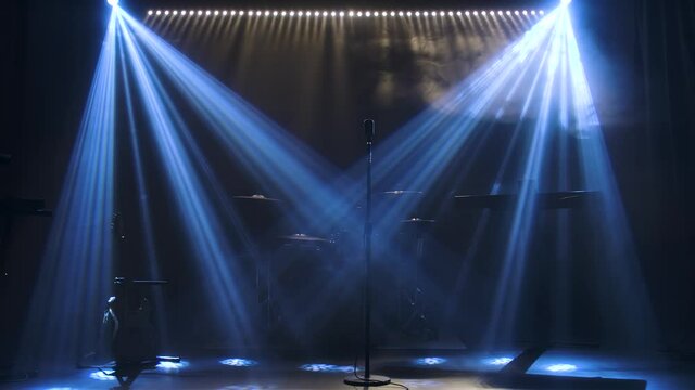 Classic retro chrome microphone and electric guitar together with drums and piano synthesizer keyboard on the stage in dark studio with smoke and neon lighting. Dynamic blue neon lighting effects
