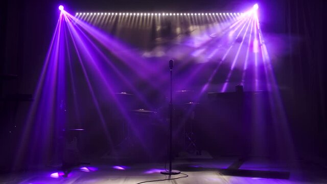 Classic retro chrome microphone and electric guitar together with drums and piano synthesizer keyboard on the stage in dark studio with smoke and neon lighting. Dynamic blue neon lighting effects