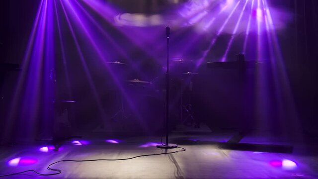 Classic retro chrome microphone and electric guitar together with drums and piano synthesizer keyboard on the stage in dark studio with smoke and neon lighting. Dynamic purple neon lighting effects