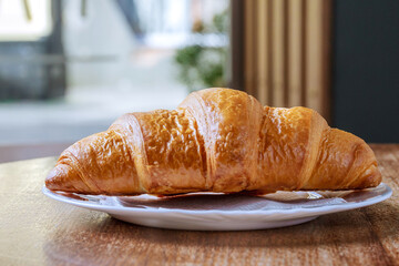 Fresh croissant on a white plate on a wooden table in a coffee shop.