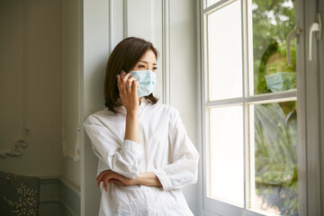 young asian woman in quarantine standing by window at home making a call