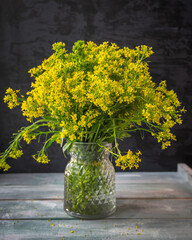 Fototapeta na wymiar Bouquet of wild flowers, blooming rapeseed in a glass vase on a thieme background