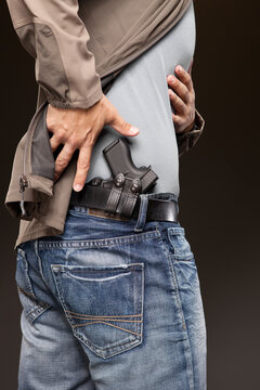 Action shot of a man who's moved his jacket aside to access his concealed carry pistol.