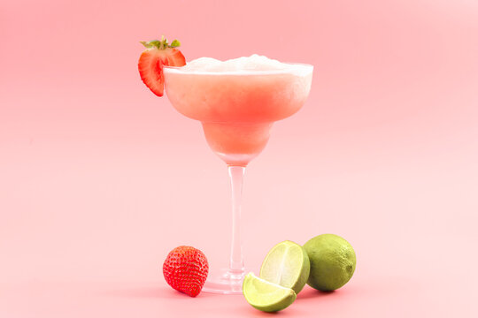 Mixed cocktails, party punch smoothies and frozen summer drinks concept with strawberry mojito or daiquiri in margarita glasses, strawberries and limes isolated on pink background