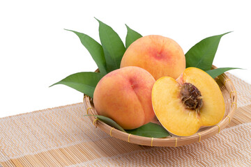 Fresh Honey Yellow Peach with leaves on bamboo mat. Sweet Golden Peach fruits on Bamboo basket isolated on white. 