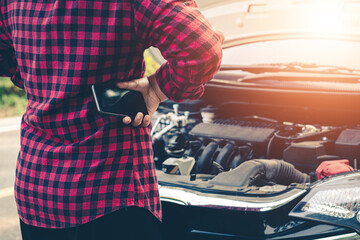 Fototapeta premium Young woman using mobile phone while looking at broken down car on road.