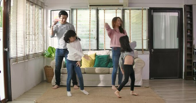 Happy family dancing with kids in living room. Young adult asian parents mom dad and cute little children daughters listening music and dance together having fun enjoying leisure lifestyle at home.