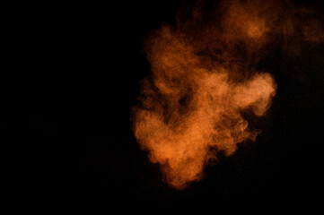 Orange powder explosion on black background. Colored powder cloud. Colorful dust explode. Paint...