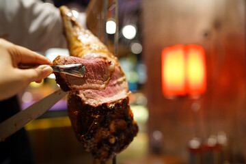 Barbecue leg of lamb on skewer - Churrasco Brazilian BBQ cooked on the rotisserie served by cutting meat directly off skewers table side, Dinner buffet seafood night.