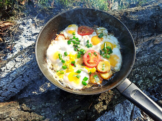 Food at the stake. Fried eggs with tomatoes in a frying pan cooked over the fire.
