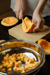 Woman chopping pumpkin on kitchen board, only hands visible. Autumn seasonal vegetables cooking. Healthy eating habits, organic vegetarian food concept.