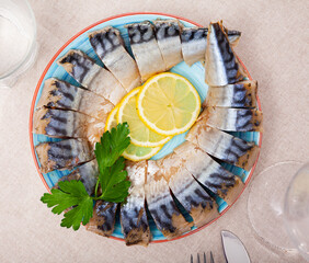 Traditional Russian appetizer of smoked mackerel fillets slices served with lemon and greens