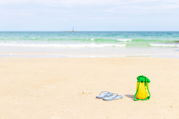 Flip-flop sandals and knitting bag on the beach; summer vacation and travel concept.