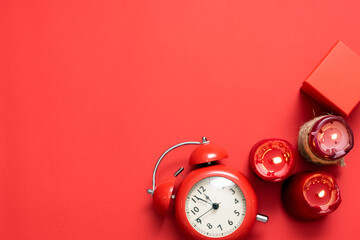 Red alarm clock, gift box and burning candles on the red flat lay background.