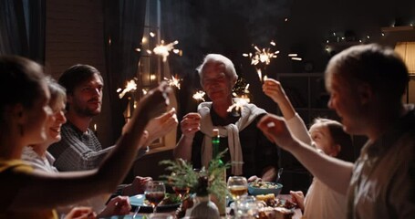 Happy family celebrating christmas at home. Family members together at holiday dinner holding sparklers, positively smiling - celebration, real people, christmas 4k footage