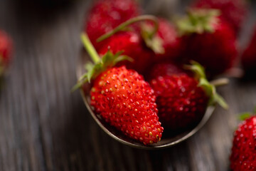 Red ripe wild strawberry in old vintage spoon on the rustic background. Selective focus. Shallow depth of field.
