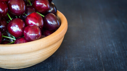 Fresh cherry berries in a light clay bowl on a dark rustic wooden background with a copy of the space
