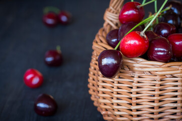 Fresh cherry berries in a wicker basket on a dark rustic wooden background with a copy of the space