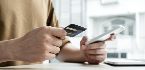 The businessman's hand is holding a credit card and using a smartphone for online shopping and internet payment in the office