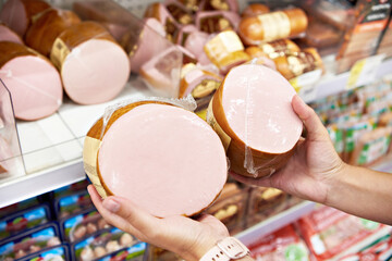 Boiled sausage in hands buyer in shop