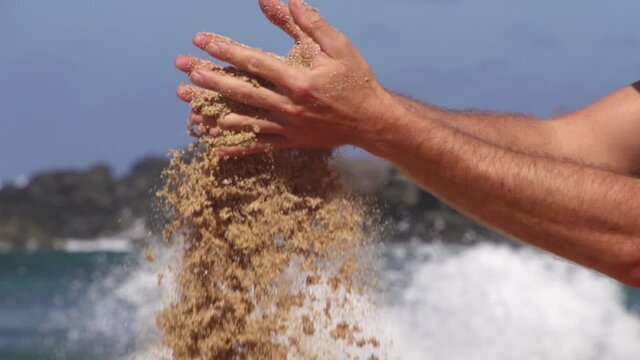 Sand falling from hands of man in super slow motion at the beach in Ho'okipa Maui Hawaii. 