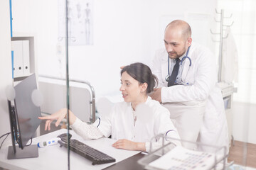 Obraz premium Team of young doctors working together on computer in hospital room. Medics wearing coats and stethoscope.